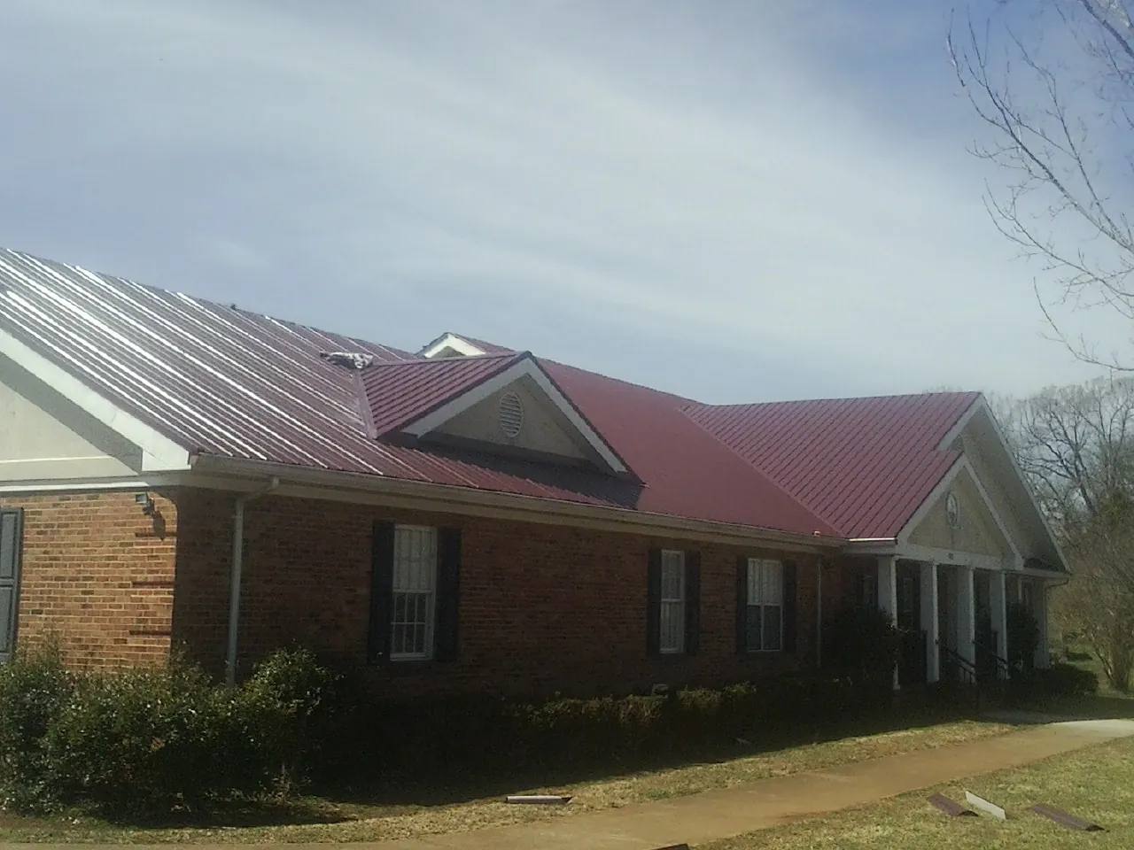 Red metal roof with gabled entries on a long brick building, from a Hail Damage Roof Repair job in Newburgh