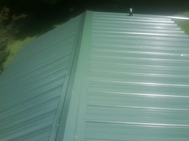 New green metal panels meeting at the ridge of a roof — Flat Roof Repair work by our crew in Newburgh
